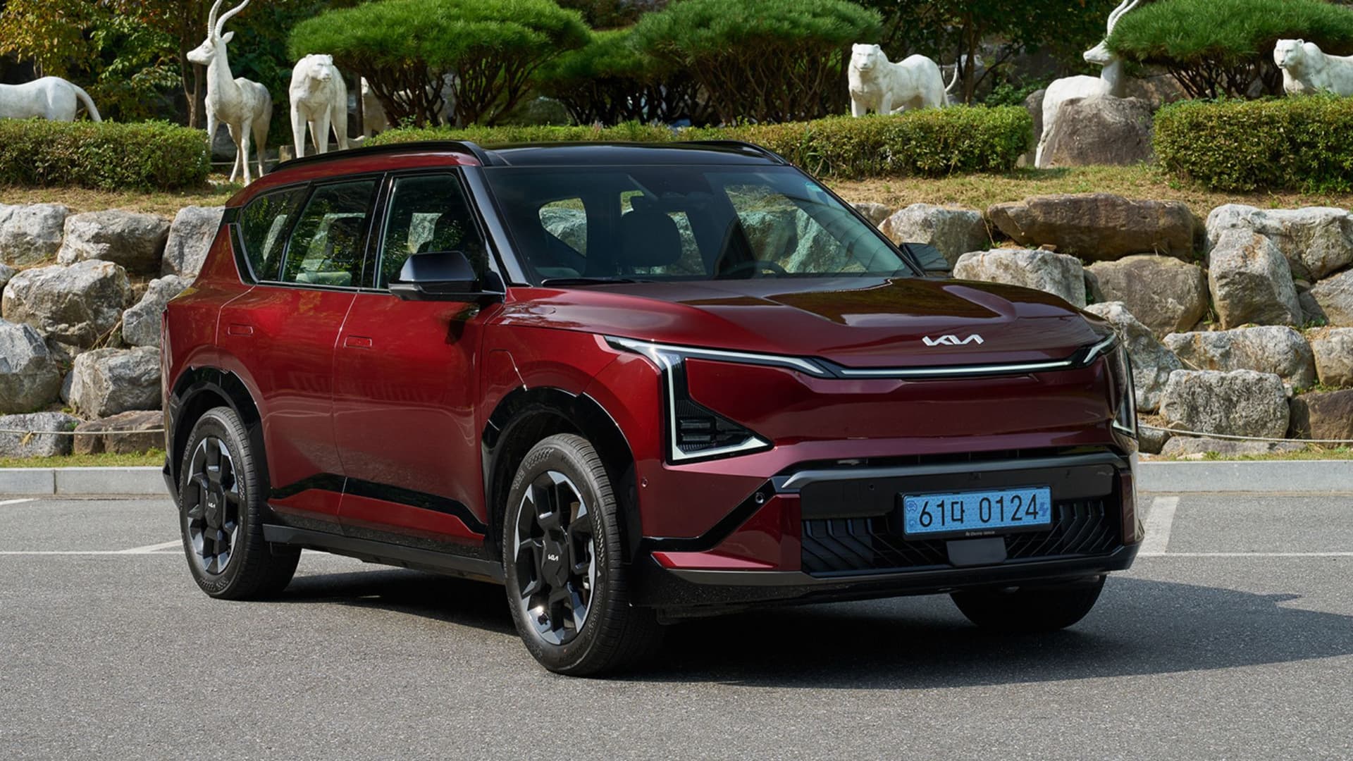KIA EV5 rouge vue de trois quarts avant sur route avec statues animales en arrière-plan